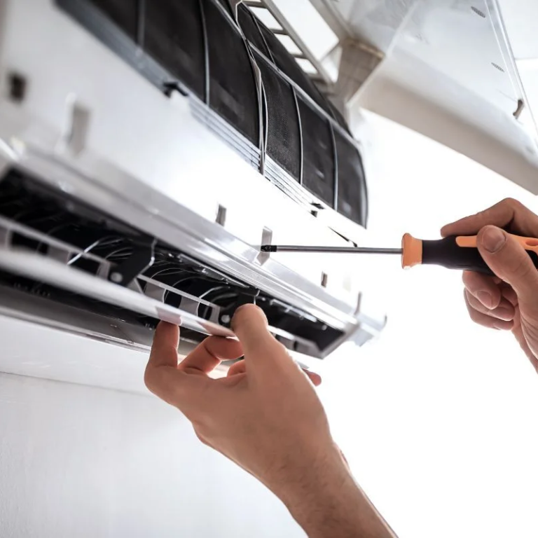 Main d'une personne utilisant un tournevis pour entretenir un climatiseur.