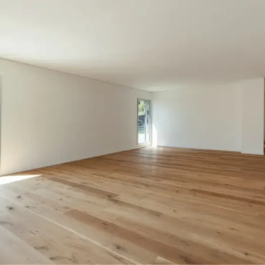 Intérieur d'une pièce vide avec un sol en bois clair et de grandes fenêtres.