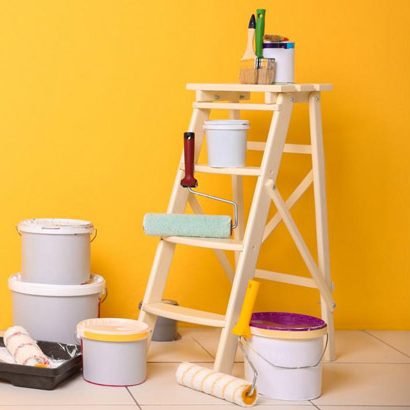 Échelle en bois avec pots de peinture et rouleau sur fond jaune.