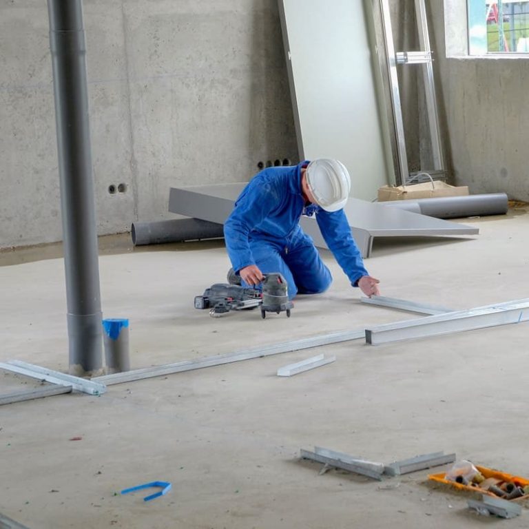 Ouvrier en bleu utilisant une scie à main sur un chantier de construction.