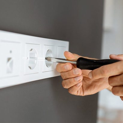 Main en train de visser une prise électrique sur un mur gris.